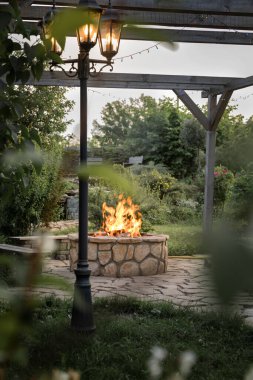 Akşamları ateş çukurunda veranda ve ateş. Güzel bir ateş alevi, parlayan bir fener ve bir akşam bahçesinin arka planında bir çelenk. Güzel bir yaz akşamı..