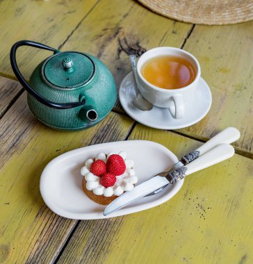 Krem peynirli çilekli vanilyalı turta. Yaz kafesinde çaydanlık ve bir fincan çay. Yukarıya bak. Hiç kimse.