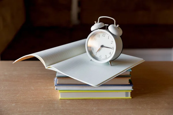 A stack of books, an open notebook and an alarm clock. Morning, the beginning of a new day of knowledge. The rising sun is reflected in the glass. Concept back to school.