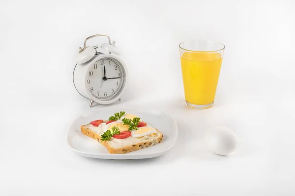 A plate with a sandwich with egg, tomatoes and parsley on the background of the clock. Near a glass of juice. Healthy food concept. Space for text