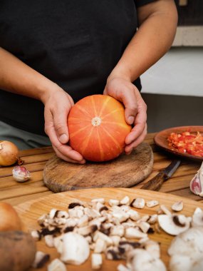 Kadınların elleri parlak turuncu bir balkabağını tutuyor. Masada sebzeli fırında balkabağı hazırlamak için malzemeler var. Yemek pişirme süreci. Bir dizi çerçeve. Sonbahar tarifleri