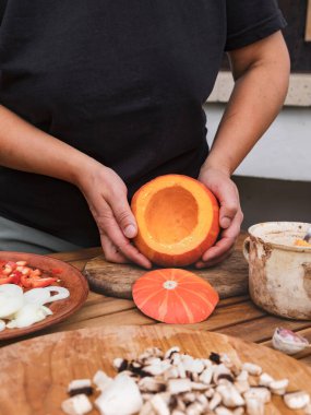 Eller temizlenmiş bir kabağı tutuyor. Yakınlarda bir kabak, mantar, sarımsak, soğan ve dolmalık biber var. Cadılar Bayramı tarifi. Vejetaryenler için sebze tabakları serisi