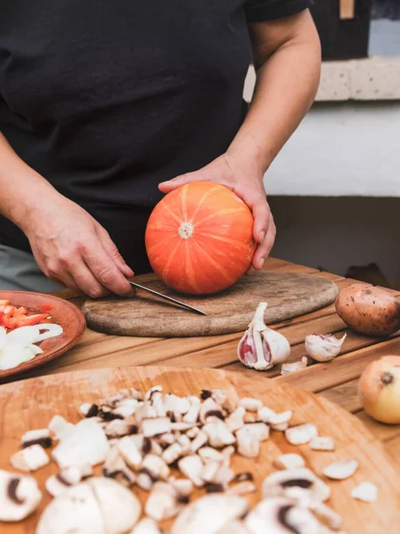 Bir kadın elinde balkabağı ve bıçak tutuyor. Cadılar Bayramı için balkabağı yemeği hazırlama süreci. Yanında doğranmış sebzeler ve şampiyonlar var. Fotoğraf serileri