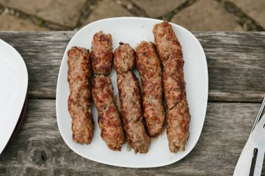 Ahşap arka planda bir tabak ızgara kebap. Üst Manzara. Barbekü sosisleri ateşte sunuluyor. Ateşin üstünde iştah açıcı yemek. Doğada hafta sonu tatili. Geçmiş kopyala