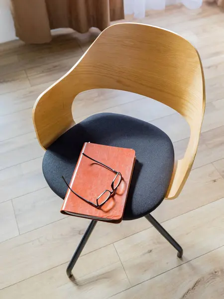 Black-rimmed glasses and a leather-bound ginger weekly book lay on an office chair. Top view. Copy space