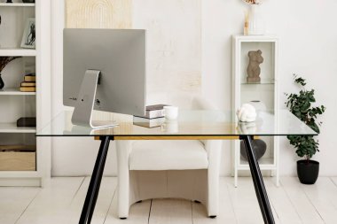 Modern bir stüdyo dairede rahat bir ofis masa, bilgisayar, kitaplar, dekor, saksıda çiçekler ve rahat beyaz deri bir koltuk.