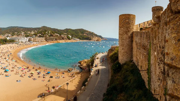 Tossa de Mar 'ın ana plajı ve kale duvarı manzarası. Badia de Tossa Körfezi. Turkuaz denizin kıyısındaki geniş kumlu sahil.