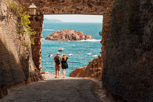 Tossa de Mar, Katalonya, İspanya 'daki Villa Vella kalesinin kapısındaki turistler. Arkadaki Badia di Tossa Körfezi ve L 'Illa Adası.