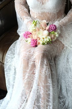 Dantelli beyaz bir peignoir giymiş genç bir gelin elinde bir buket çiçek tutuyor. Dantel elbiseli bir kızın kucağında düğün buketi. Çiçekçiden güzel tasarımcı buketi