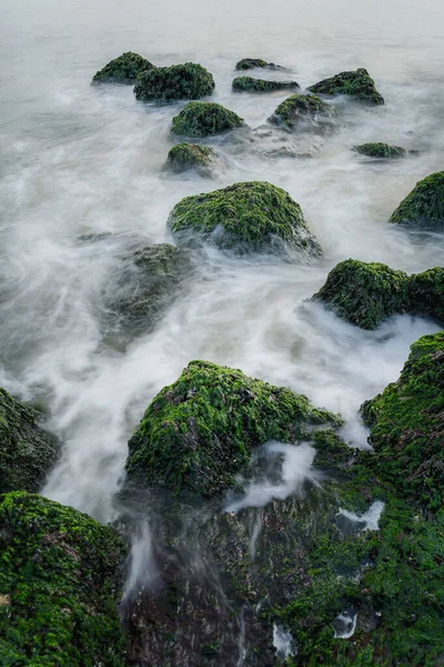 stock image North Sea coast at nightly light and long exposure, under sinking sun irradiates bricks and stones in seawater, moving lake and foaming waves on shore.