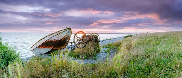 stock image Rowing boat on slipway with hoist mechanism along the dyke of the IJsselmeer with red colored rain clouds drifting over the lake