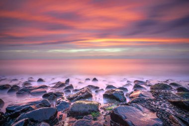 Deniz kıyısında gün batımı. Batı Kapelle, Zeeland, Hollanda 'da, pastel gökyüzünün altındaki kaya oluşumlarına çarpan dalgaların çarpıcı görüntüsü