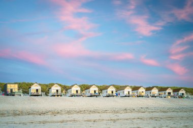 Small cabins against a row of dunes with a beautiful evening sky during sunset on the beach clipart