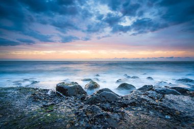 Deniz kıyısında gün batımı. Batı Kapelle, Zeeland, Hollanda 'da, pastel gökyüzünün altındaki kaya oluşumlarına çarpan dalgaların çarpıcı görüntüsü
