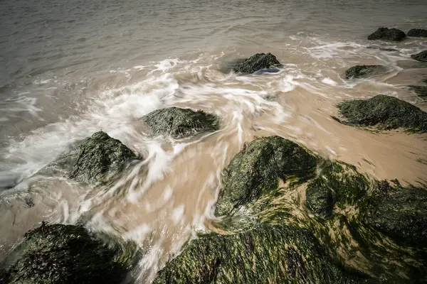 Tide flows in and out over rocks at low tide. Fast stream, water runs over stones. Long exposure