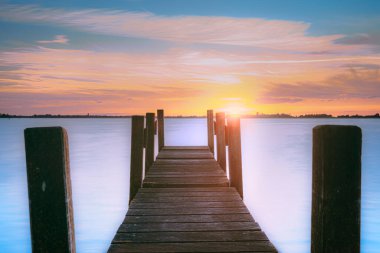Su ve göl, ahşap iskeleli (iskele), ufukta batan güneş ve güzel renklerde bulutlu gökyüzü. Hollanda 'nın kırsal bölgeleri, Giethoorn
