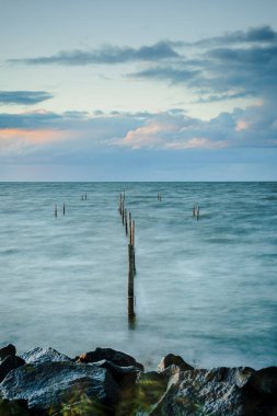 Ön plandaki kayalar fotoğrafta güzel bir derinlik yaratırken kutuplar seni renkli gökyüzüne yönlendiriyor. IJsselmeer, Hollanda