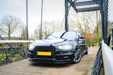 Siyah dört kapılı araba, açık havada metal bir asma köprüye park edilmiş..