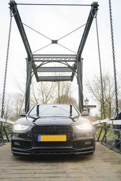 Siyah dört kapılı araba, açık havada metal bir asma köprüye park edilmiş..