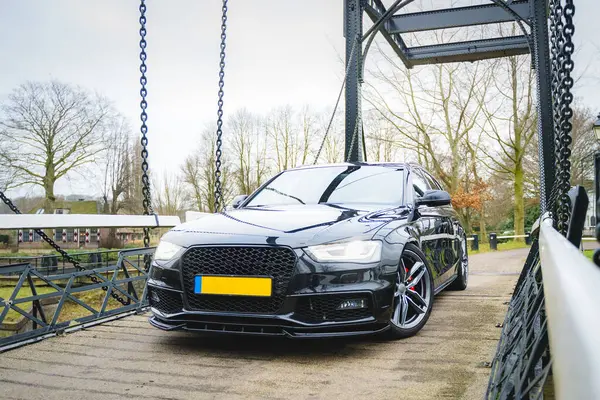 Siyah dört kapılı araba, açık havada metal bir asma köprüye park edilmiş..