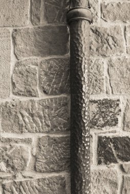 Taş bir duvarın arka planındaki eski drenaj borusu.