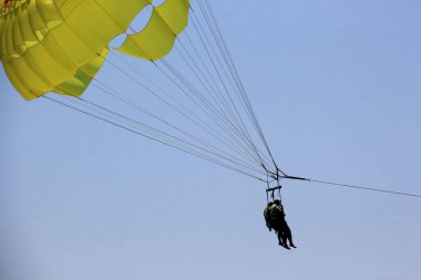 Budva plajı yakınlarında mavi bir gökyüzünde paraşüt, insanlarla dolu sarı bir paraşüt.