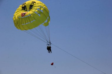 Budva plajı yakınlarında mavi bir gökyüzünde paraşüt, insanlarla dolu sarı bir paraşüt.