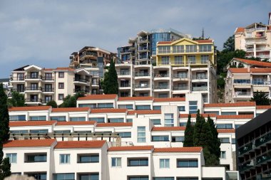  Budva, Karadağ - 25 Haziran 2023: Otel ve apartmanlı tepe, önünde saman plaj şemsiyeleri, Eski Budva plajı, Karadağ                              
