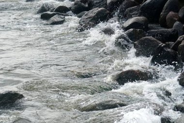 Deniz suyu kıyıdaki siyah kayalara sıçrar.                               