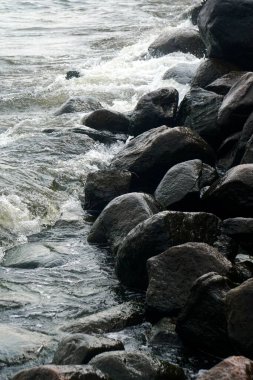 Deniz suyu kıyıdaki siyah kayalara sıçrar.                               