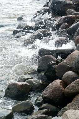 Deniz suyu kıyıdaki siyah kayalara sıçrar.                               