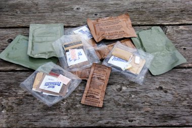 Riga, Latvia, - 23 June 2024 : Several Individual Food Rations for USA soldiers. Pack of Meal, Ready to Eat (MRE) food, USA army military food kit on an old wooden board background clipart