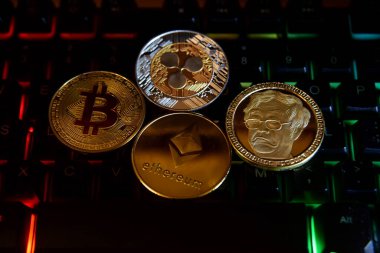 Bitcoin hatıra paraları. Altın Bitcoin, Ripple ve Ethereum madeni paraları bir bilgisayar klavyesinde, renkli ışıkla aydınlatılmış. dijital ödeme sistemi