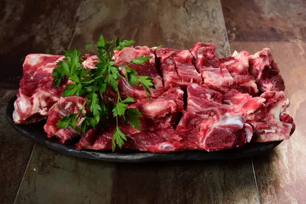 Siyah kil tabakta etli çiğ sığır kemikleri, kahverengi taş arka plan. Et suyu seçimi
