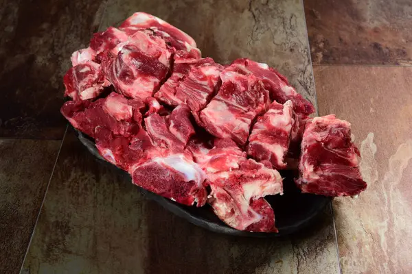 Siyah kil tabakta etli çiğ sığır kemikleri, kahverengi taş arka plan. Et suyu seçimi