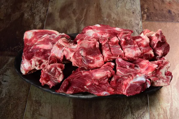 Siyah kil tabakta etli çiğ sığır kemikleri, kahverengi taş arka plan. Et suyu seçimi