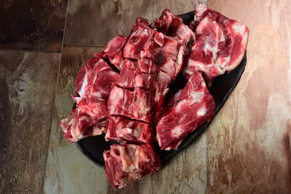 Siyah kil tabakta etli çiğ sığır kemikleri, kahverengi taş arka plan. Et suyu seçimi