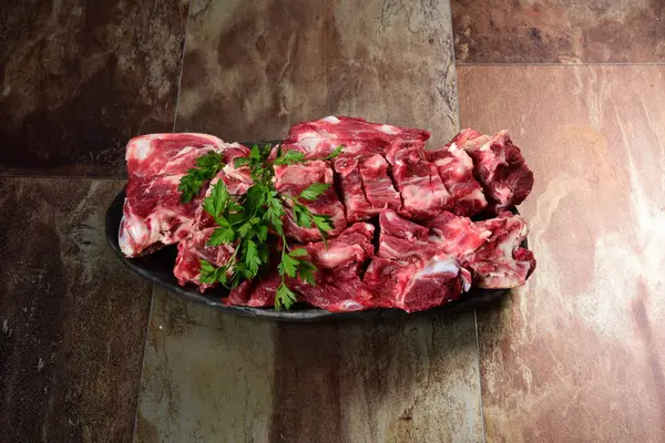 Siyah kil tabakta etli çiğ sığır kemikleri, kahverengi taş arka plan. Et suyu seçimi