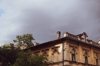 Eski püskü ve terk edilmiş bir ev. Ağır gri bulutların altında, sıcak renklerde.