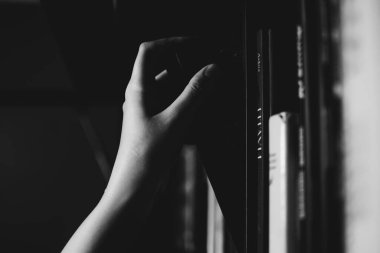 Raftan siyah kitap seçen bir kızın soluk beyaz eli. Edebiyat, okuma, okur yazarlık ve bilgi kavramı. Siyah ve beyaz