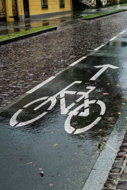 Islak asfalt yolda bisiklet yolunda parlak beyaz bir işaret. Ekim 'de soğuk yağmurlu bir gün.