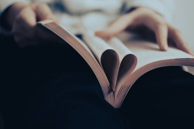 Kavram: Romanlara ve edebiyata aşık olmak. Kalp şeklinde kitap sayfaları bir okuyucunun ellerinde.