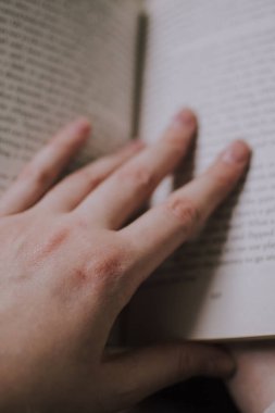 Kitap okuyan ve narin parmaklarıyla çizgileri takip eden bir kız.
