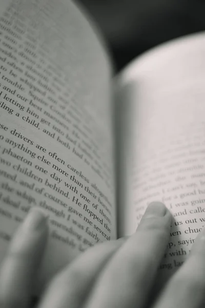 一个女孩读一本书 用苍白柔嫩的手指沿着线条走下去的黑白照片 — 图库照片