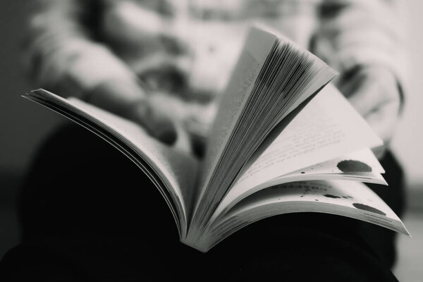 Bleak black and white colors of an open book in the hands of a reader with blurred background
