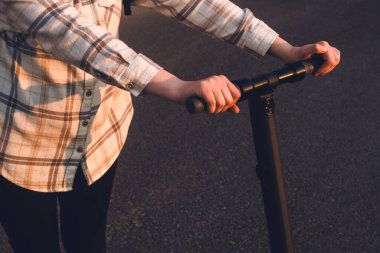 Gün batımında elektrikli scooterını tutan bir kız.