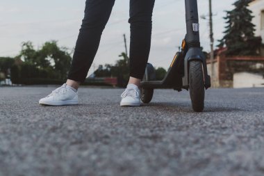 Modern aktif Wooman bir yaz akşamında elektrikli scooterının yanında duruyor.