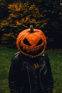 Siyah deri ceket giyen bir adamın portresi ve bir balkabağı feneri kostümü.