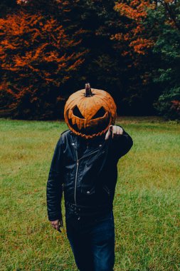 Siyah deri ceketli bir adam ve kamerayı işaret eden bir balkabağı kostümü. Cadılar Bayramı ruhu kavramı