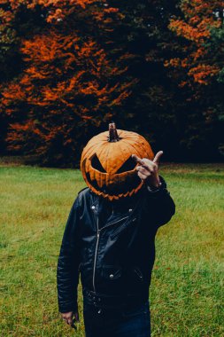 Siyah deri ceket giyen ve orta parmağını kameraya gösteren bir balkabağı kostümü giyen adam. Cadılar Bayramı ruhu kavramı